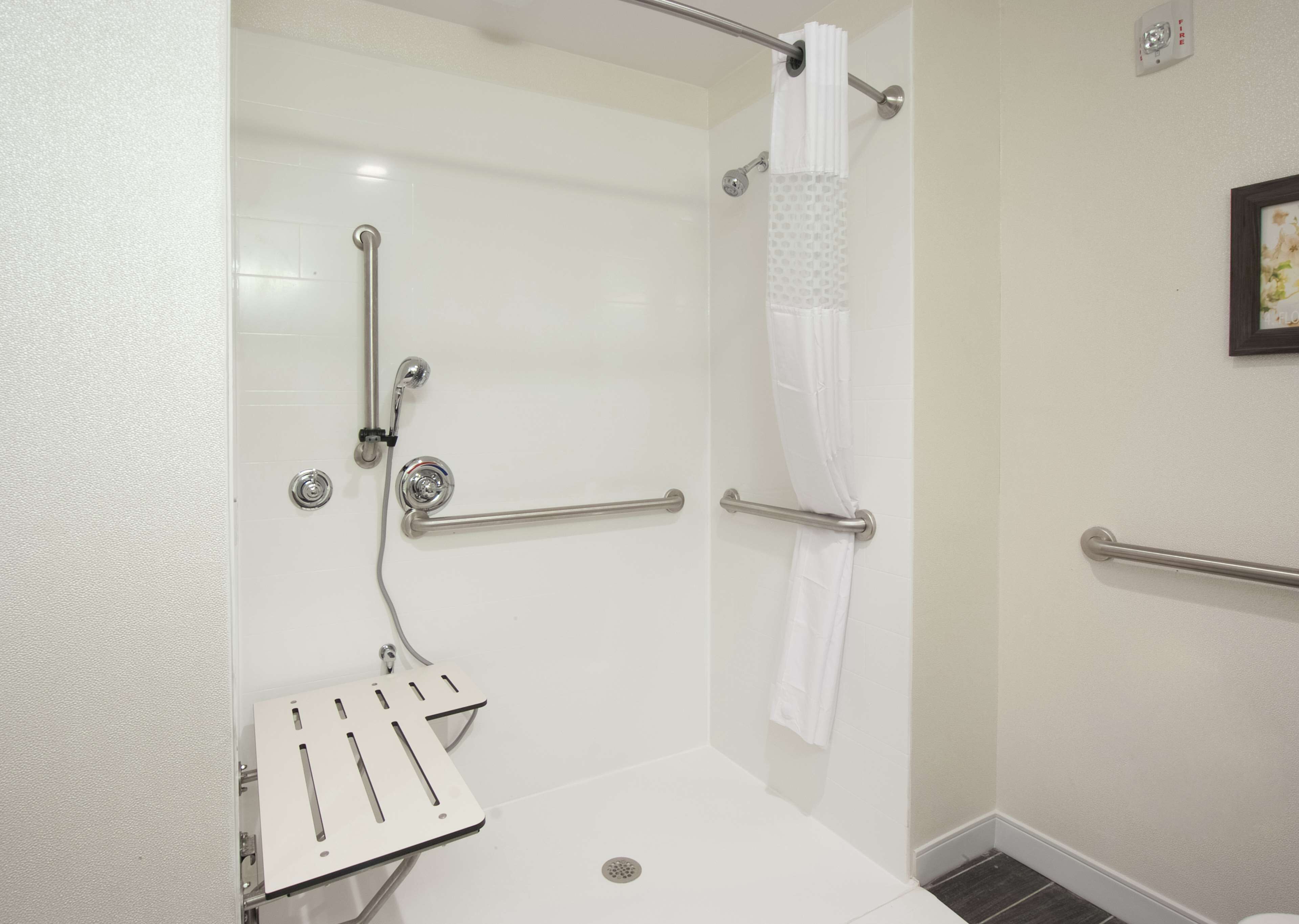A modern bathroom with a walk-in shower, grab bars, and a white toilet.