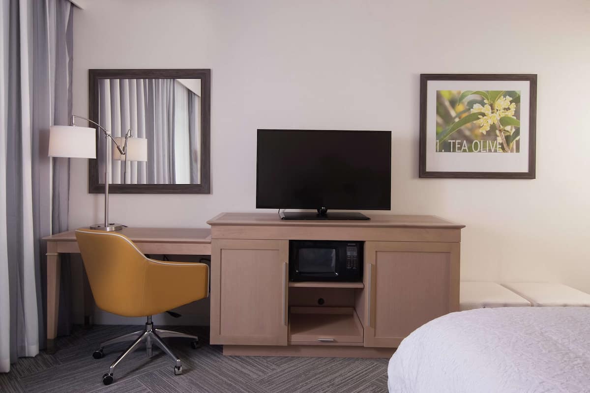 Habitación de hotel con escritorio, televisión, microondas, una silla amarilla y cama.