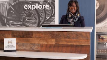 A reception desk with a wooden panel design, a sign for Hilton HHONORS, and a background featuring bicycles and a refrigerator with Celeste brand products.