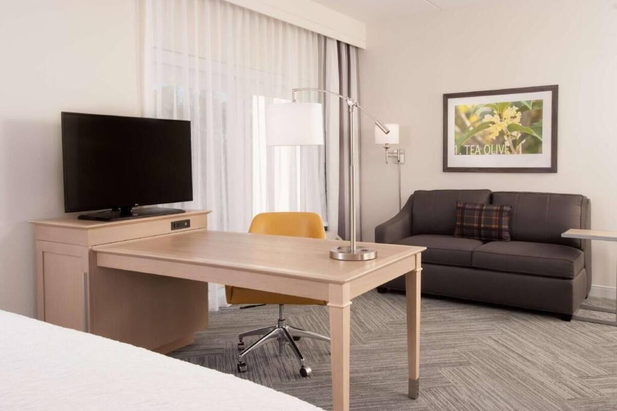Habitación de hotel con cama, escritorio con televisor, sofá, lámpara y un cuadro en la pared.