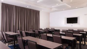 Un salón de conferencias con mesas y sillas, un ventanal grande y un televisor de pantalla plana en la pared.