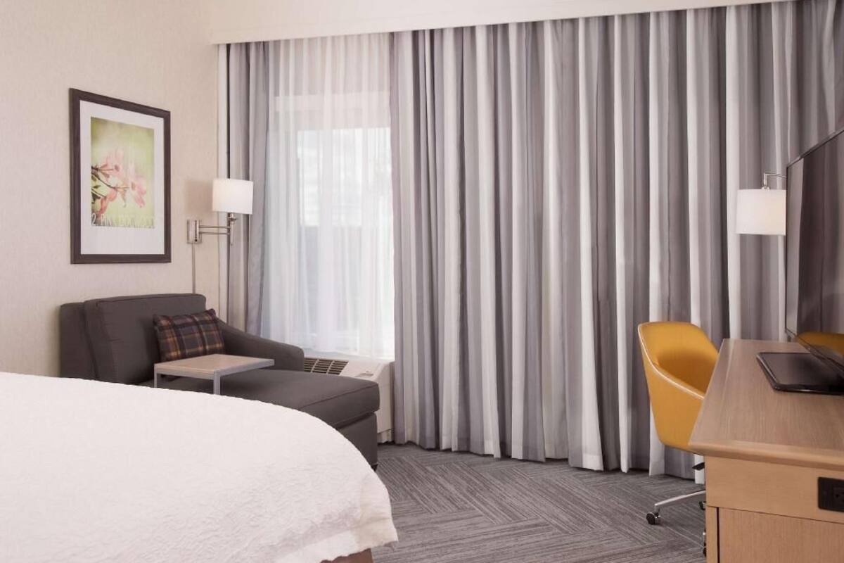 Habitación de hotel con cama, escritorio, silla, sofá, mesita y ventana con cortinas.