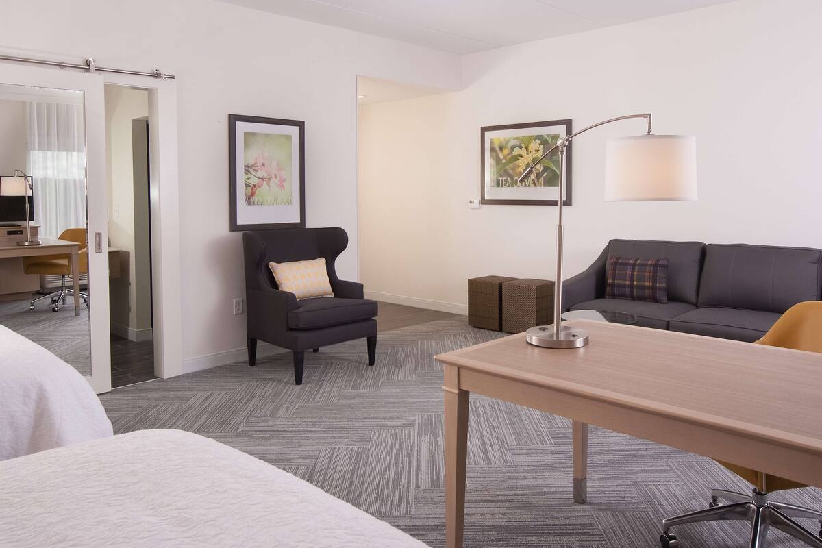Habitación de hotel con cama, escritorio, sillón, sofá y dos cuadros en la pared.