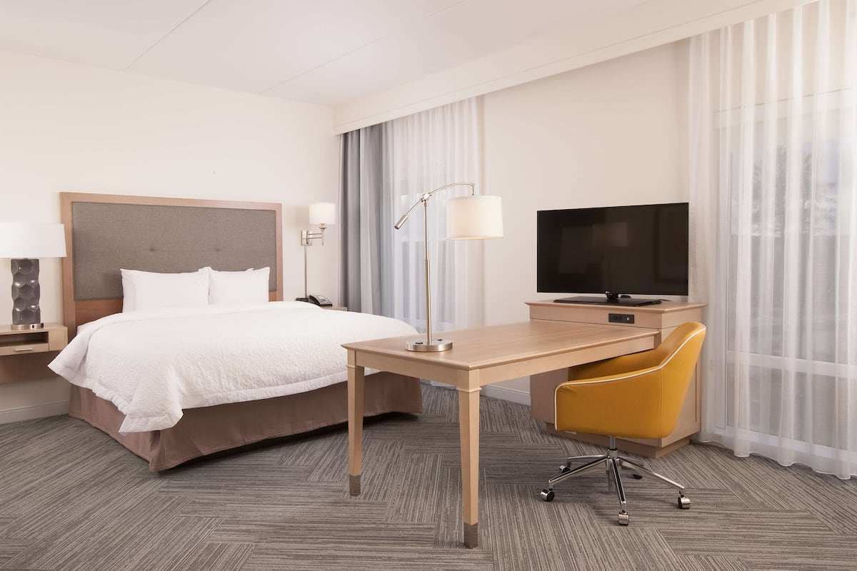 Una habitación de hotel con cama, escritorio, silla, televisor y lámpara.