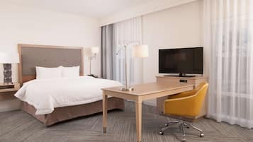 Una habitación de hotel con cama, escritorio, silla, televisor y lámpara.