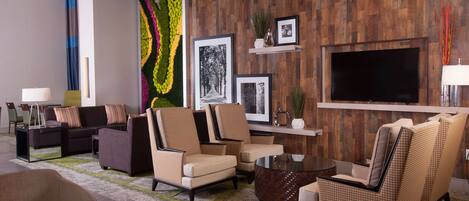 A modern living room with sofas, armchairs, a coffee table, and a flat-screen TV mounted on a wooden wall.