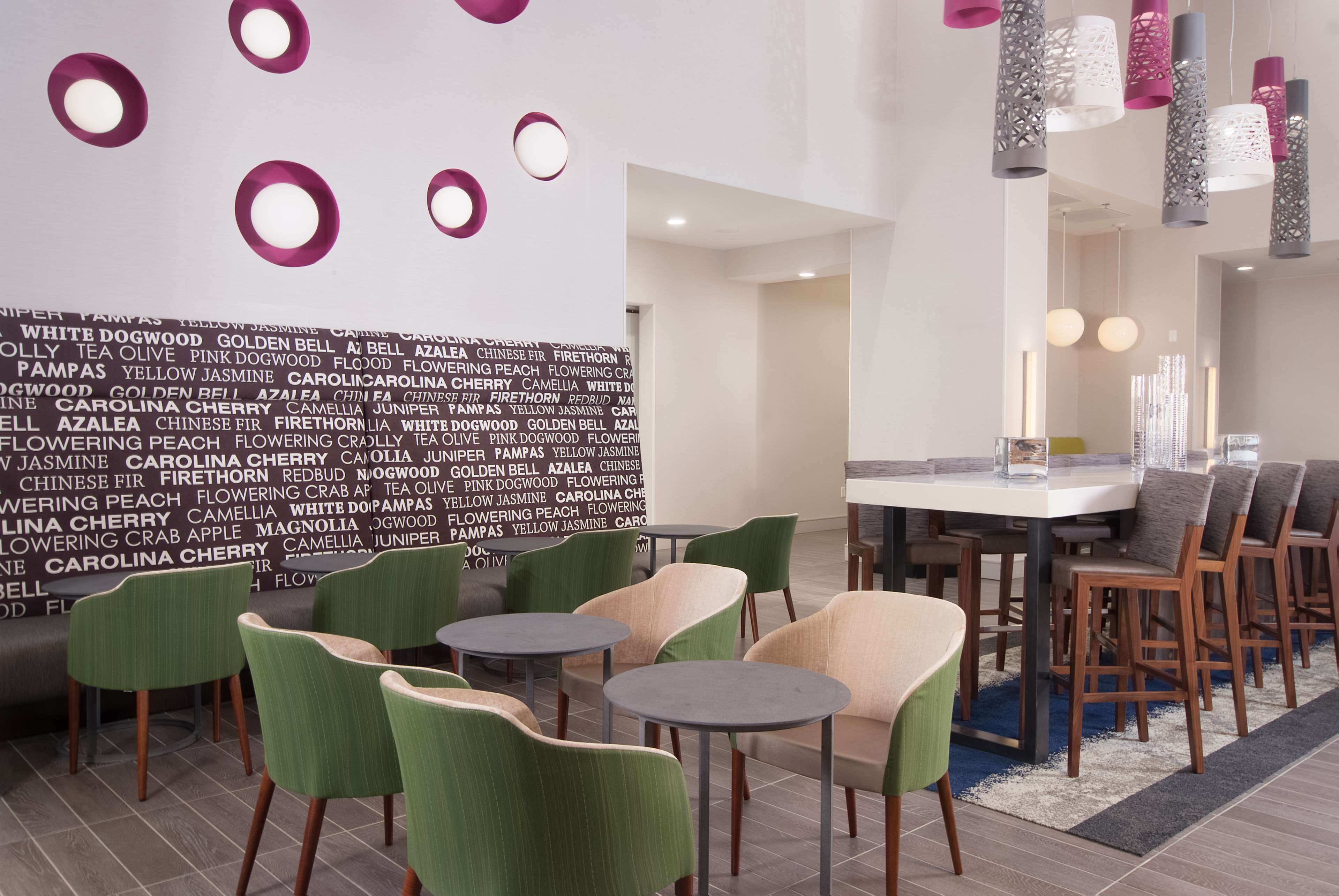 A modern hotel lobby with a dining area featuring round tables and chairs, a wall with text, and decorative lighting.
