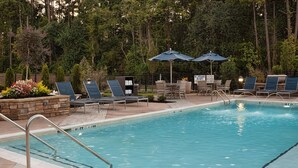 A swimming pool with lounge chairs and umbrellas, surrounded by trees.