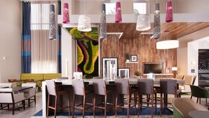 A modern hotel lobby with a dining area, a large wall mural, and contemporary lighting fixtures.