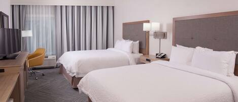 A hotel room with two beds, a desk, a chair, a TV, and a window with curtains.