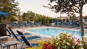 A pool area with lounge chairs and a small table, surrounded by greenery and flowers.