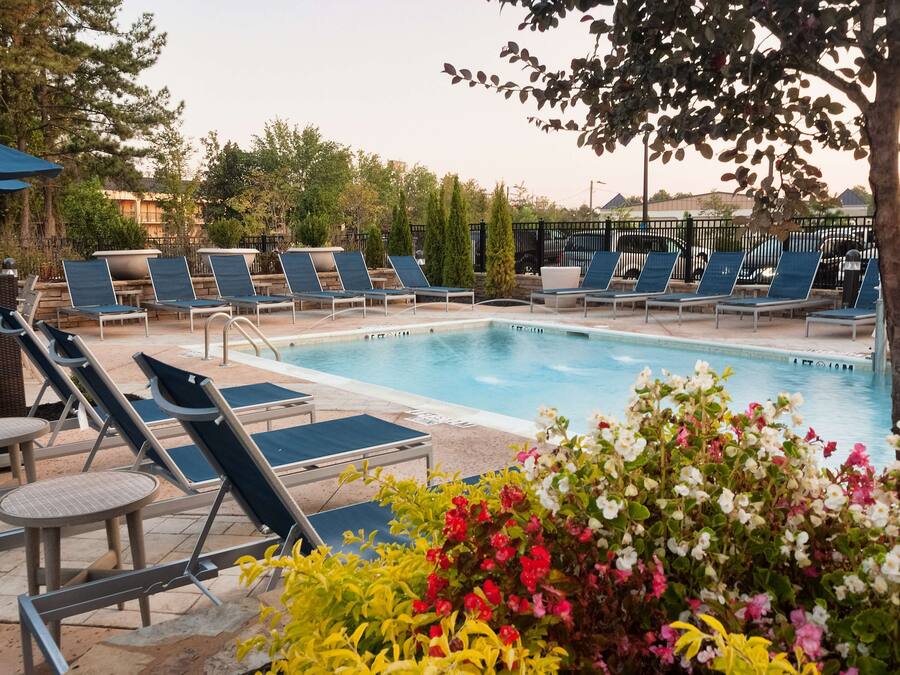 A pool area with lounge chairs and a small table, surrounded by greenery and flowers.