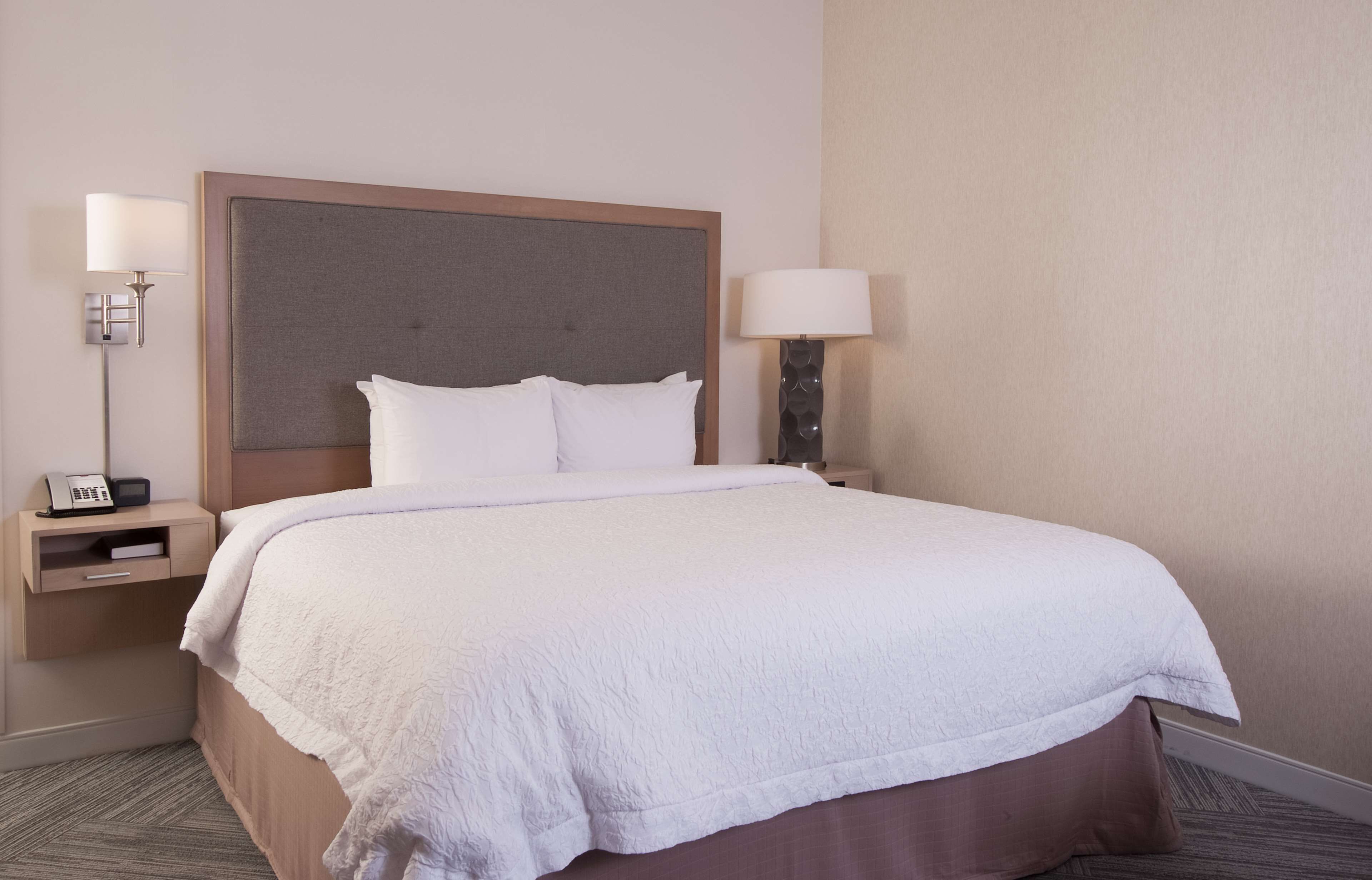 A neatly made bed with a large headboard, two bedside tables with lamps, and a telephone on one of the tables.