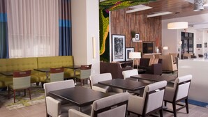 A modern hotel lobby with a yellow sofa, dining tables, and chairs.