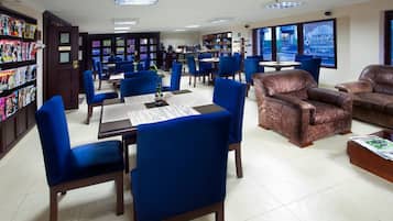 Une bibliothèque avec des chaises bleues, un canapé en cuir marron et une table sur laquelle se trouve un livre.