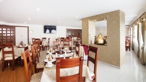 A spacious dining area with multiple tables and chairs, a television mounted on the wall, and a decorative wall piece. - Hotel Fernando Plaza (San Juan de Pasto)