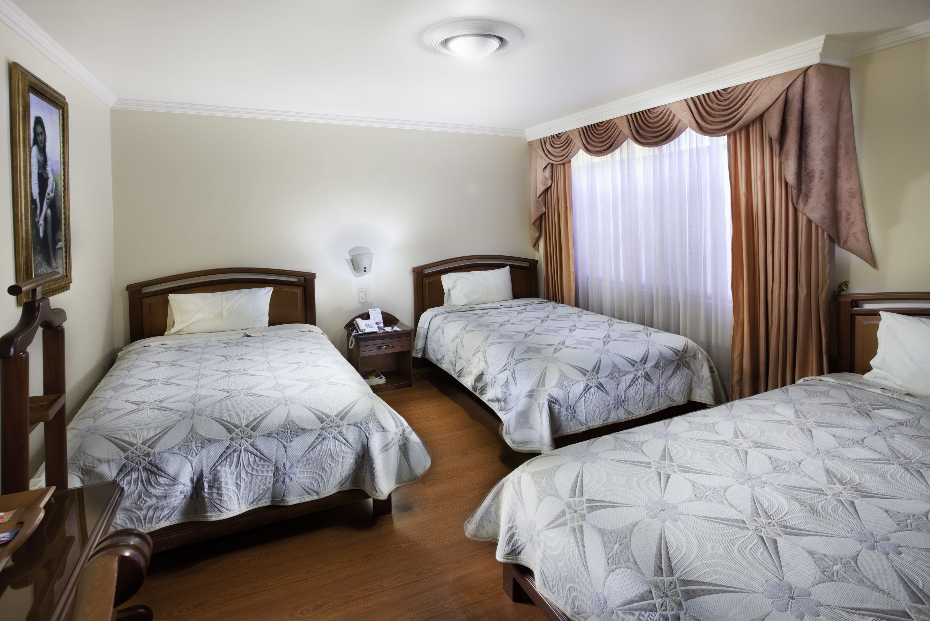 A hotel room with two beds, wooden headboards, a nightstand, and a framed picture on the wall.
