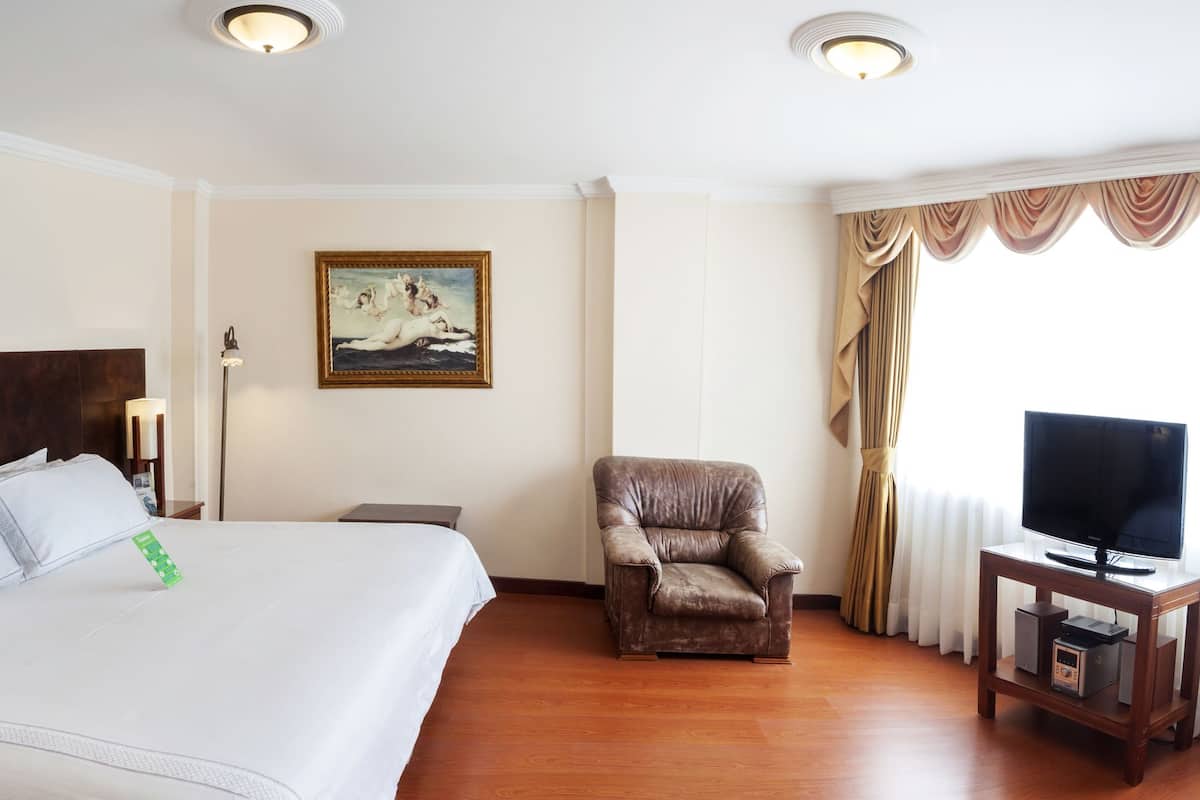 A hotel room with a large bed, a chair, a TV on a wooden stand, and a painting on the wall.