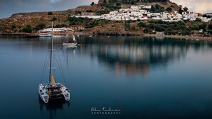 Un pueblo costero con un castillo en una colina, aguas tranquilas y barcos.