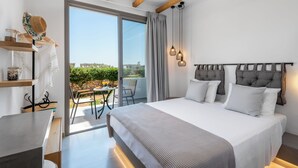 Habitación de hotel moderna con una cama grande, un balcón con mesa y sillas, y vista a la ciudad.