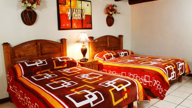 Una habitación con dos camas, una mesita de noche con lámpara y un cuadro en la pared.