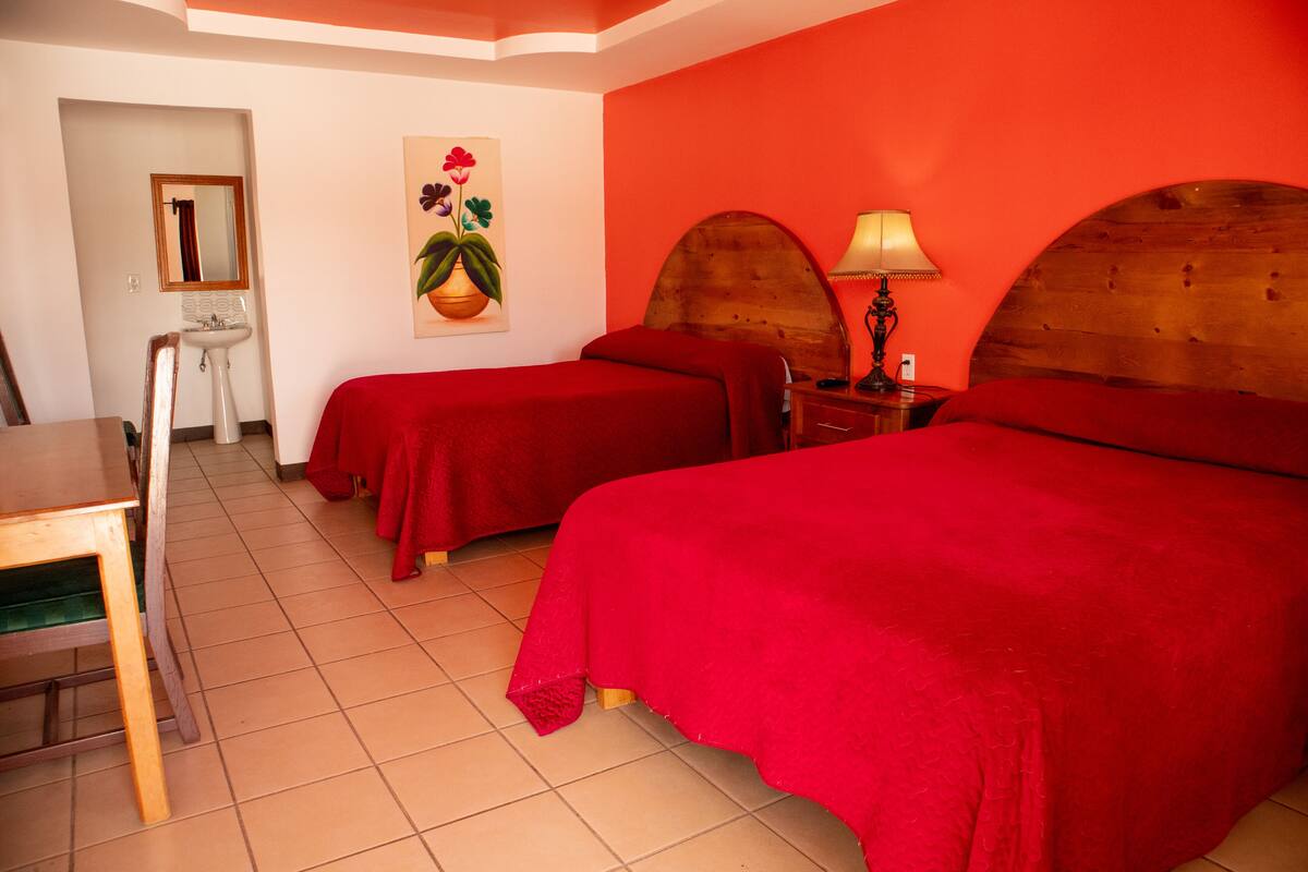 Une chambre d’hôtel avec deux lits, un bureau, une chaise, un lavabo et un miroir.