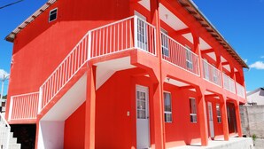 Un edificio rojo con un balcón blanco, varias ventanas y una puerta.