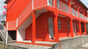 Un edificio rojo de dos pisos con balcón, escalera y puerta.
