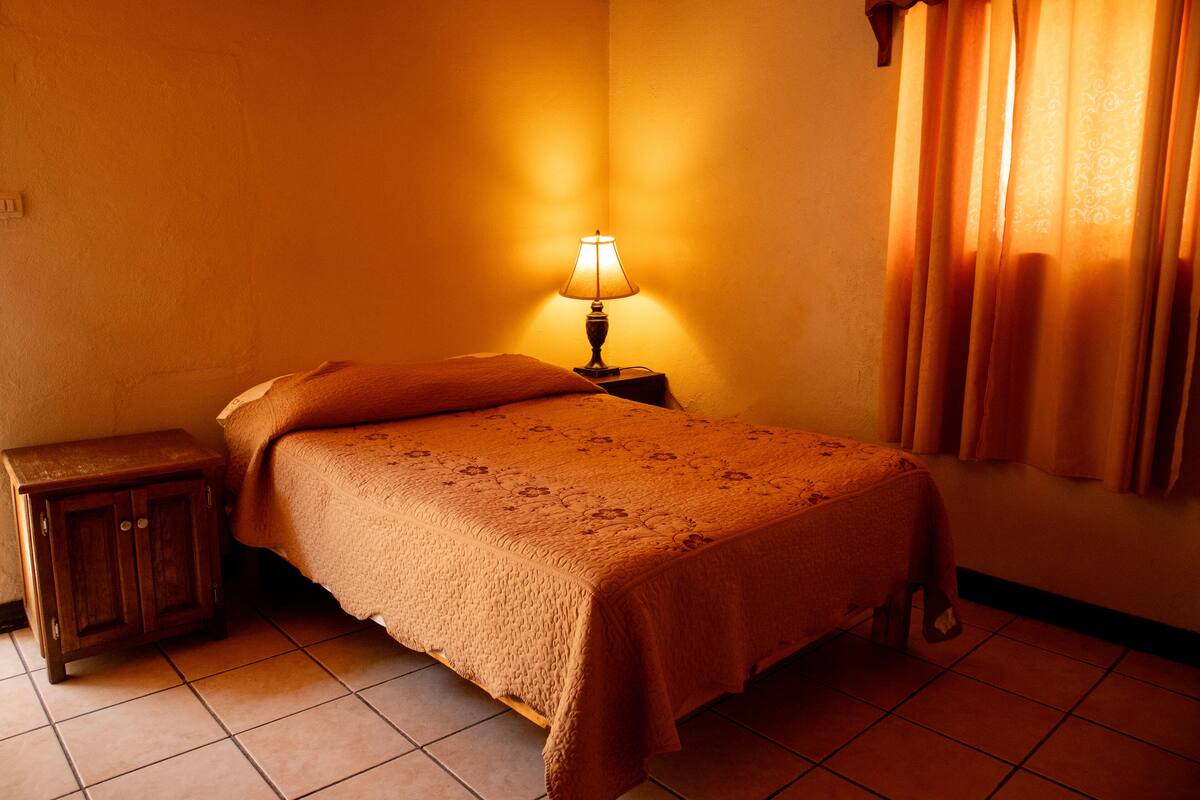 Un lit simple avec une couvre-lit à motifs, une table de chevet et une lampe.
