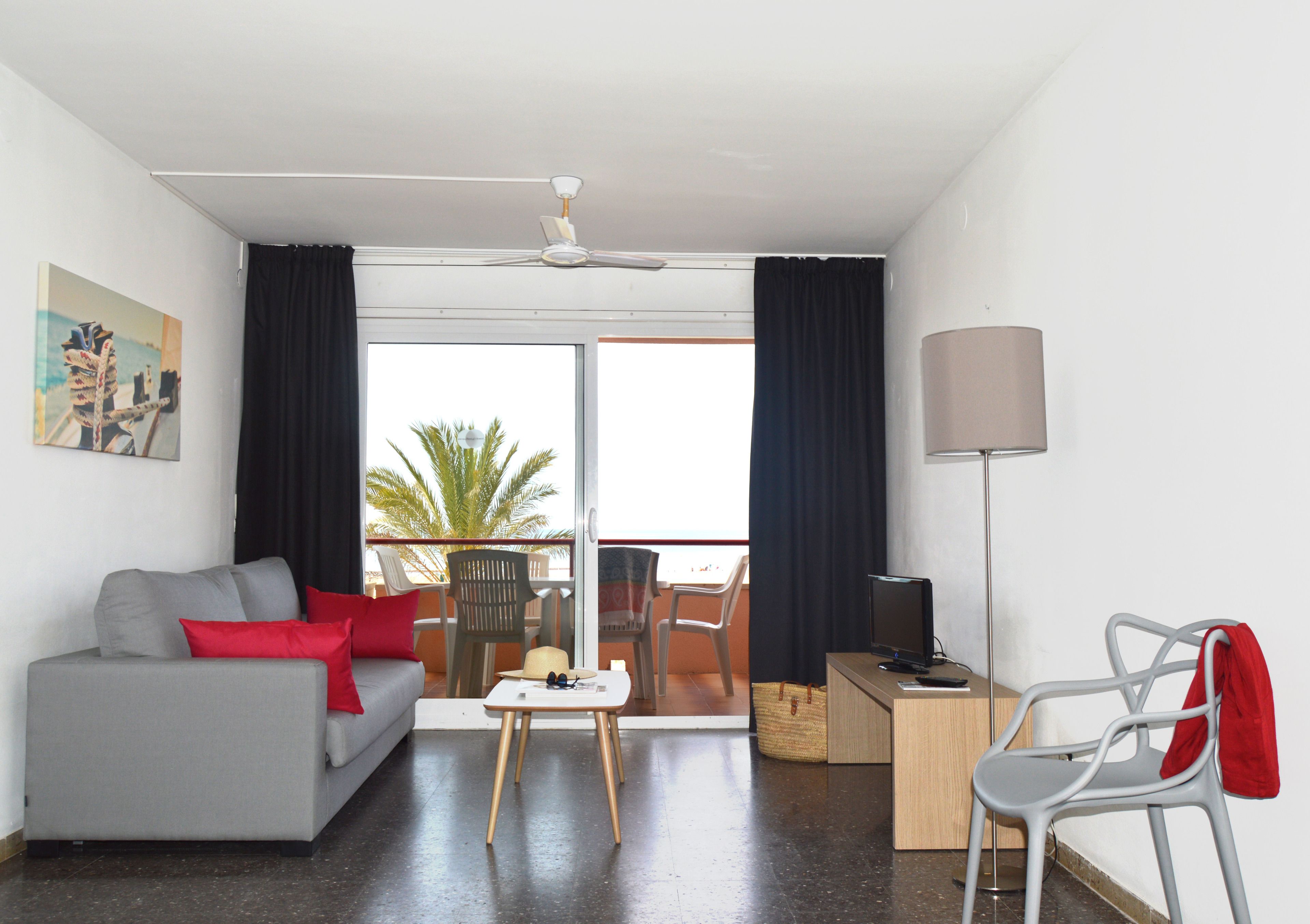 Un soggiorno moderno con un divano grigio, cuscini rossi, un tavolino, una TV su un mobile in legno e un balcone con vista.