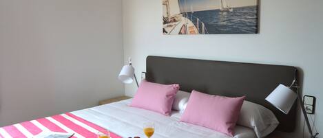 A neatly made bed with a pink and white striped bedspread, a tray with breakfast items, and a painting of a sailboat on the wall.
