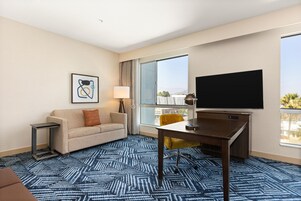 Habitación de hotel con sofá, escritorio, televisor y un amplio ventanal con vistas.