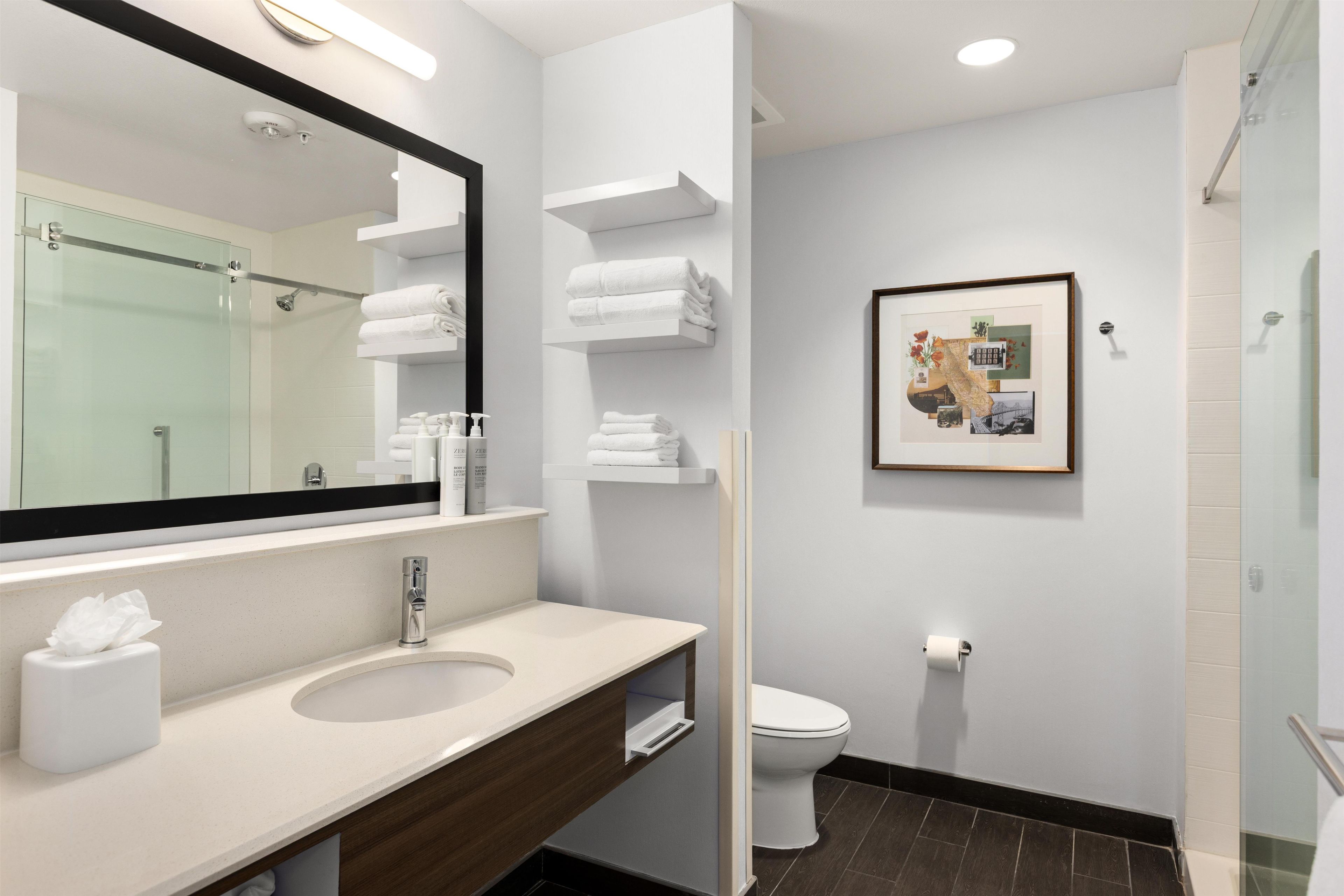 A modern bathroom with a large mirror, a sink, a toilet, and a glass shower enclosure.