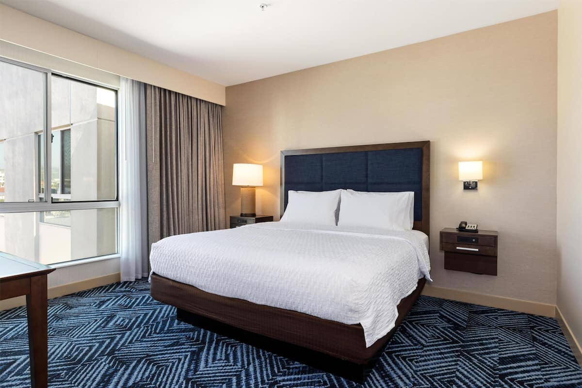 A hotel room with a large bed, two bedside tables, a desk, and a window with curtains.