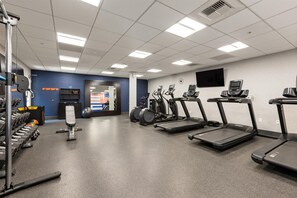 Et fitnessrum med løbebånd, crosstrainere og styrketræningsudstyr.