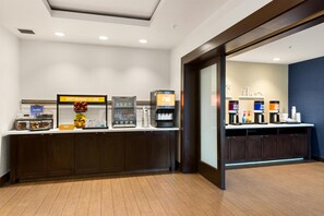 A breakfast bar with a coffee machine, a juice dispenser, and a refrigerated display case. - Hampton Inn & Suites Los Angeles - Glendale (Glendale)