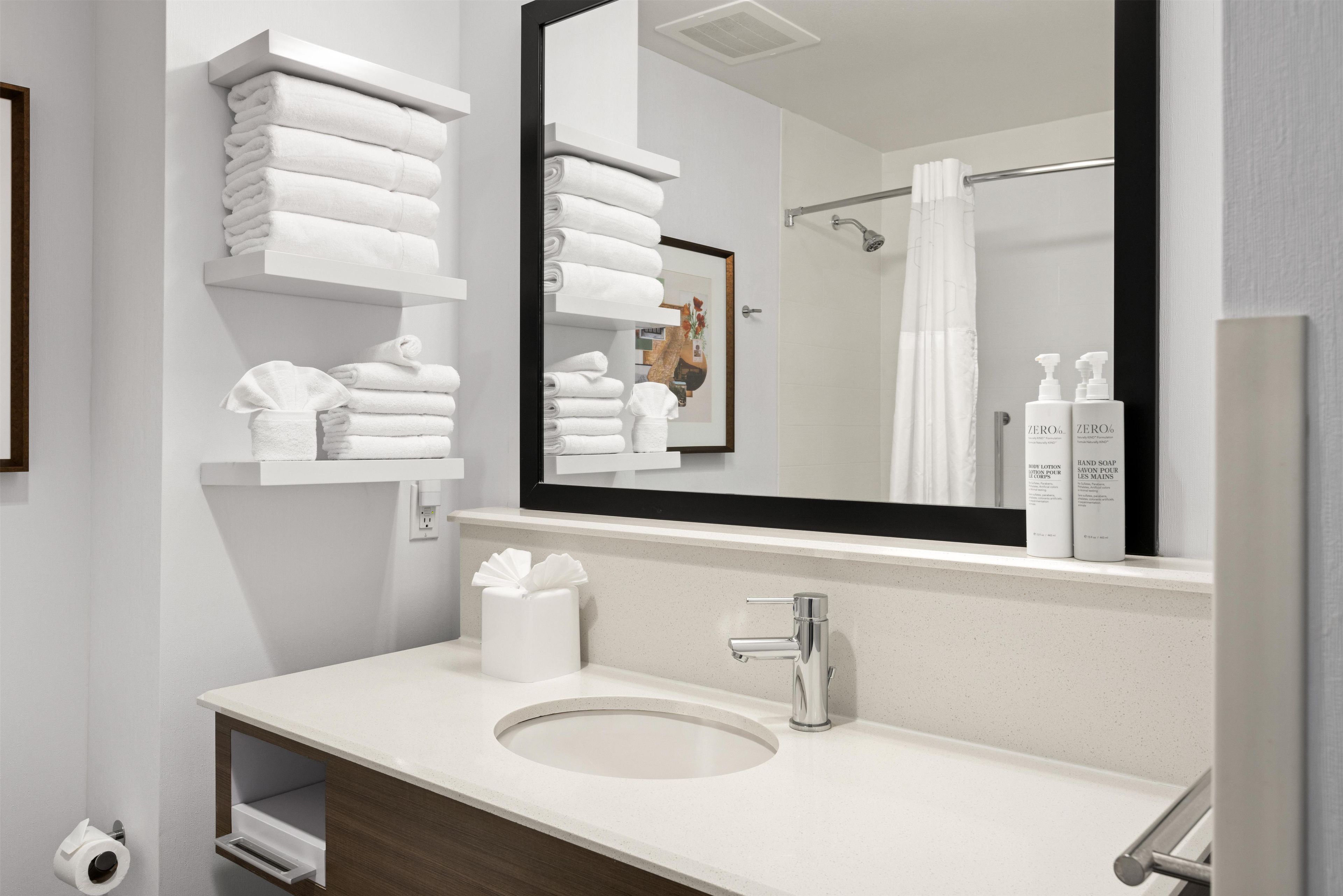 Un baño moderno con un espejo grande, toallas blancas, un lavabo y una zona de ducha.