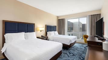 Ein Hotelzimmer mit zwei Betten, einem Fernseher, einem Schreibtisch und einem Fenster mit Vorhängen.