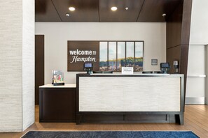 En receptionsdisk med et 'Welcome to Hampton' skilt, udsigt over bybilledet og en 'Hilton Honors' plade.
