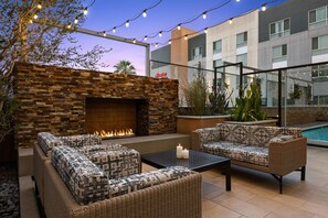 An outdoor patio with wicker furniture, a stone fireplace, and string lights. - Hampton Inn & Suites Los Angeles - Glendale (Glendale)