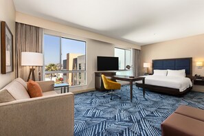 Habitación de hotel con cama, escritorio, televisor, sofá y vistas a la ciudad.