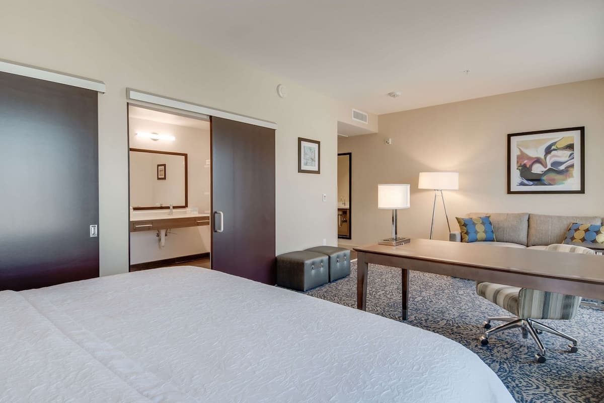 A hotel room with a large bed, a desk, a sofa, a small stool, and a mirror.