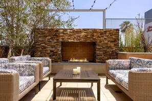 A patio area with wicker furniture, a metal table, and a brick fireplace. - Hampton Inn & Suites Los Angeles - Glendale (Glendale)