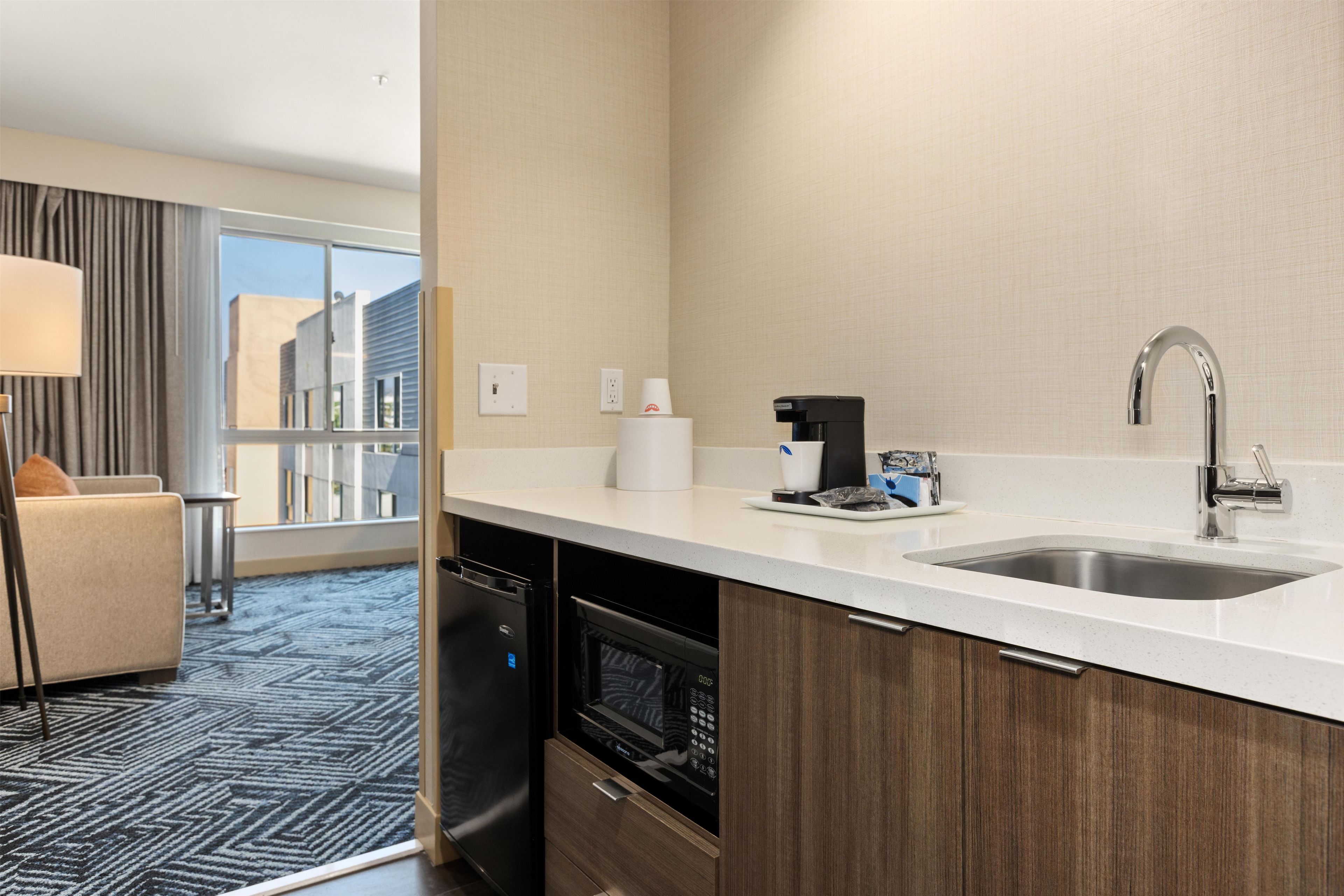 A modern hotel room with a kitchen area, including a sink, coffee maker, and dishwasher.