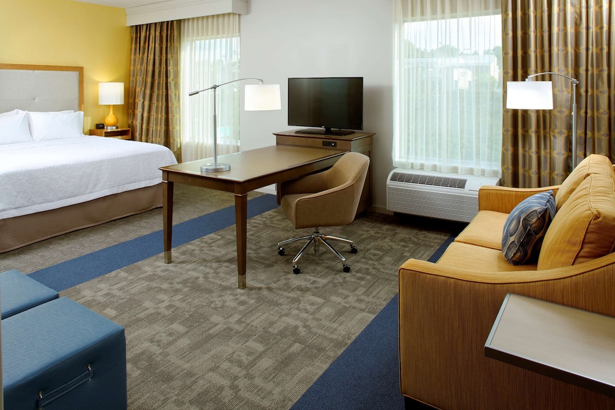 A hotel room with a bed, a desk with a TV, a sofa, and a chair.
