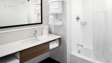 A modern bathroom with a white sink, mirror, and shower. There are towel racks and a hair dryer on the vanity.