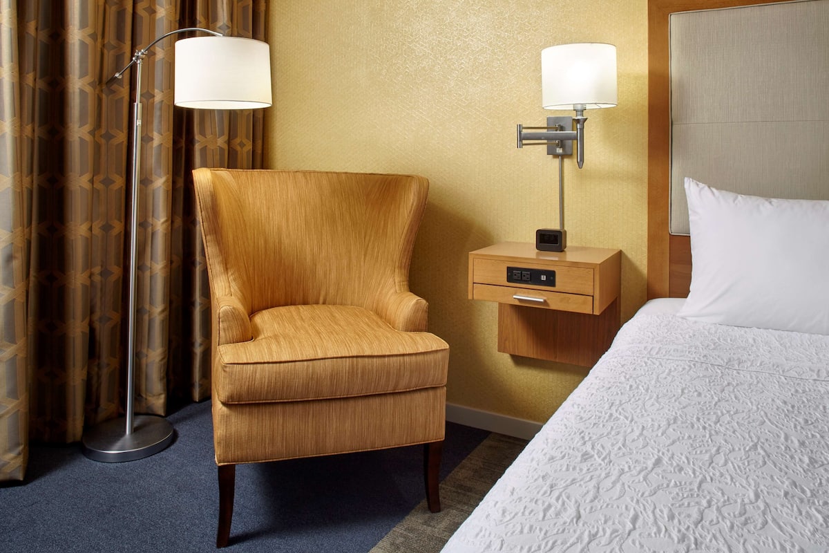 A hotel room with a single bed, a nightstand with a lamp, a chair, and a floor lamp.