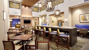 A hotel lobby with multiple dining tables and chairs, a central bar area, and a television mounted on the wall. - Hampton Inn & Suites Pittsburgh Airport South–Settlers Ridge (Pittsburgh)