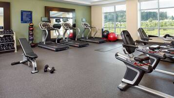 Une salle de sport équipée de tapis de course, d’un banc de musculation, d’haltères et de ballons d’exercice.