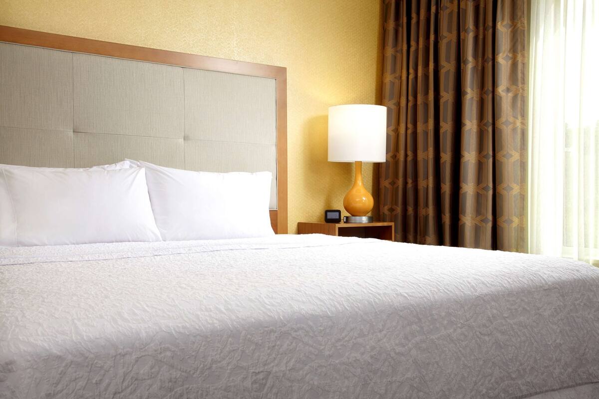 A hotel room with a large bed, a nightstand with a lamp, and a window with curtains.